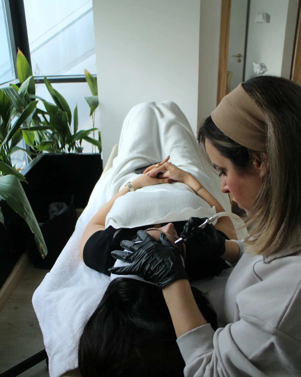 A client and a technician at the manicure table, mid-conversation, in window light.