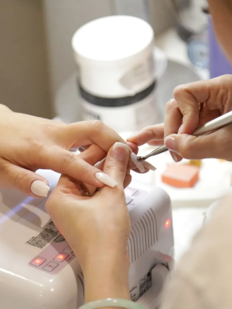 A technician shaping a client’s nails under the lamp.